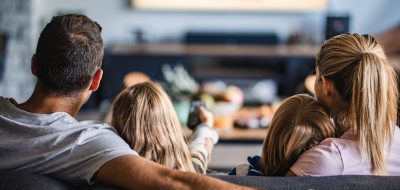 Vue arrière d'une famille détendue regardant la télévision sur le canapé du salon.